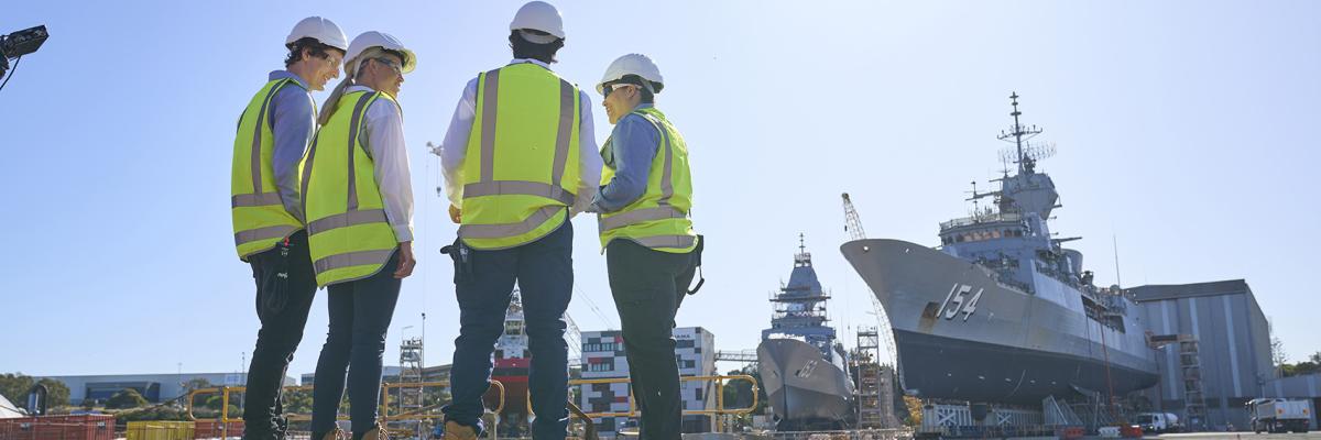Four people standing in high vis, looking at a Naval ship.