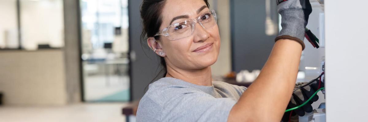 Female electrician smiling at the camera whilst plugging in wires