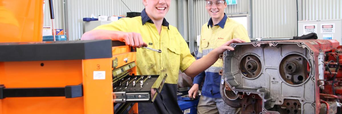 Two tradies smiling at the camera with car motor in foreground