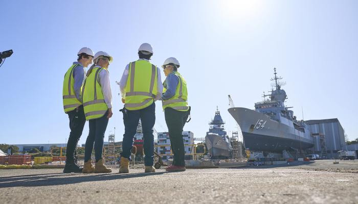 Four people standing in high vis, looking at a Naval ship.