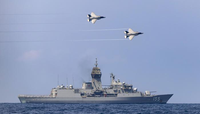Naval ship with two planes flying overhead. 