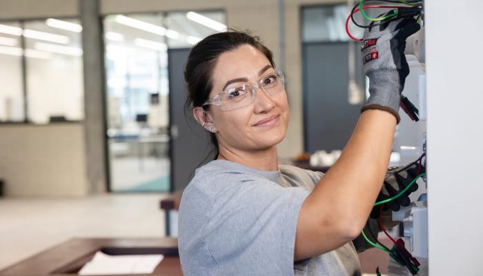 Female electrician smiling at the camera whilst plugging in wires