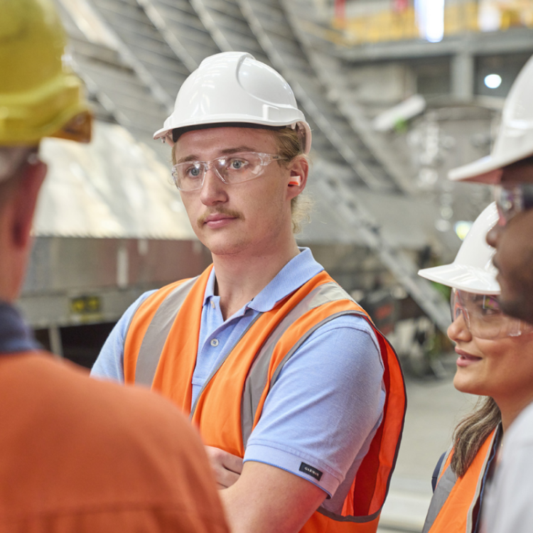 Male student listening to manager. Ship under construction in background. 
