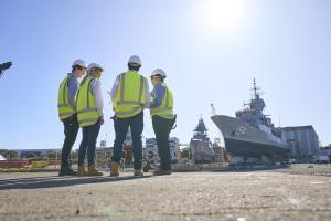 Four people standing in high vis, looking at a Naval ship.